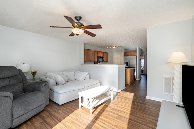 living room featuring a textured ceiling, ceiling fan, and dark wood-type flooring