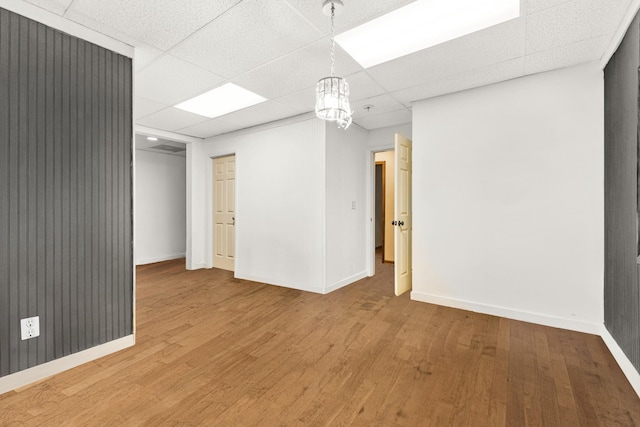 spare room with a paneled ceiling, wood-type flooring, and an inviting chandelier