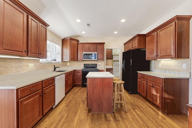 kitchen featuring sink, black appliances, light hardwood / wood-style flooring, a kitchen island, and a breakfast bar area