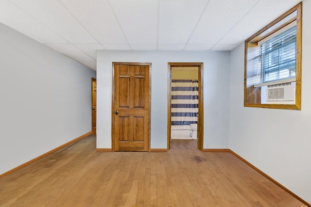 unfurnished bedroom with a walk in closet, a drop ceiling, cooling unit, and light hardwood / wood-style flooring