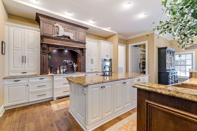 kitchen featuring light stone counters, light hardwood / wood-style floors, an island with sink, and white cabinets