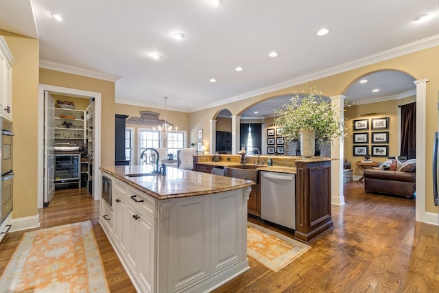 kitchen featuring sink, dishwasher, white cabinetry, hanging light fixtures, and an island with sink