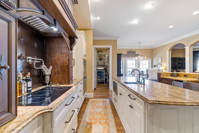 kitchen featuring sink, a kitchen island with sink, white cabinetry, black electric stovetop, and light stone countertops