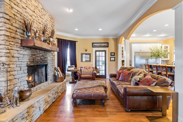 living room featuring crown molding, hardwood / wood-style flooring, and a stone fireplace