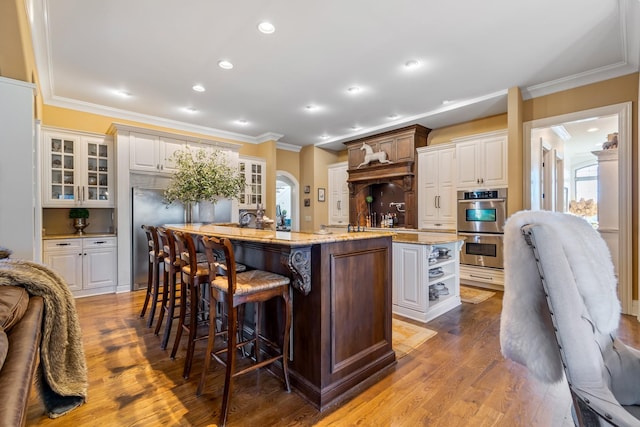 kitchen featuring light hardwood / wood-style flooring, a center island with sink, a kitchen breakfast bar, stainless steel double oven, and white cabinets