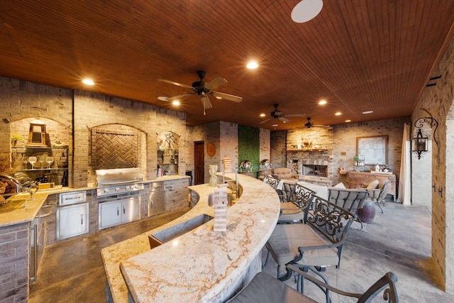 view of patio / terrace with area for grilling, a bar, ceiling fan, a grill, and an outdoor stone fireplace