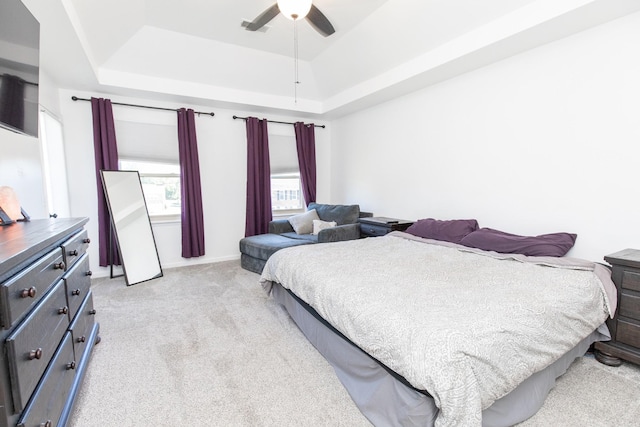 bedroom featuring ceiling fan, a raised ceiling, and light colored carpet