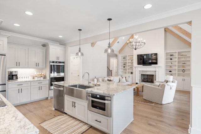 kitchen with light stone countertops, appliances with stainless steel finishes, sink, decorative light fixtures, and white cabinetry