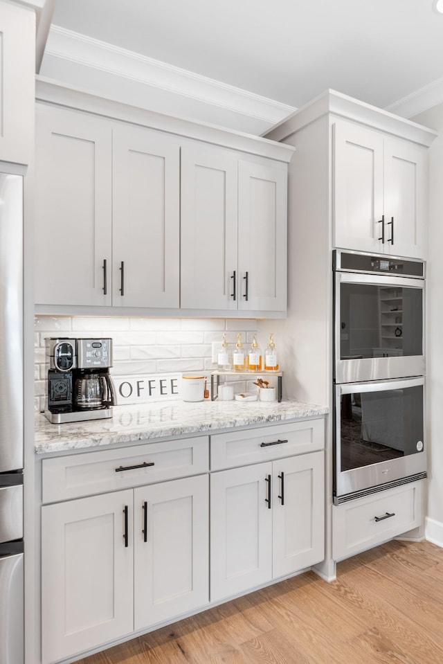 bar featuring light hardwood / wood-style flooring, white cabinetry, double oven, and crown molding