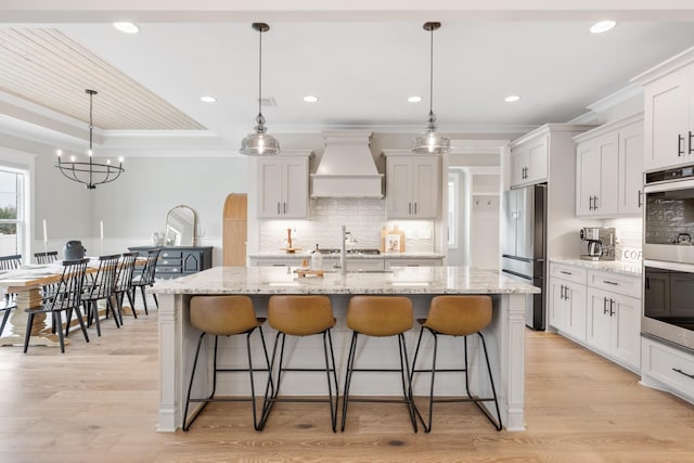 kitchen with a kitchen island with sink, pendant lighting, and custom exhaust hood