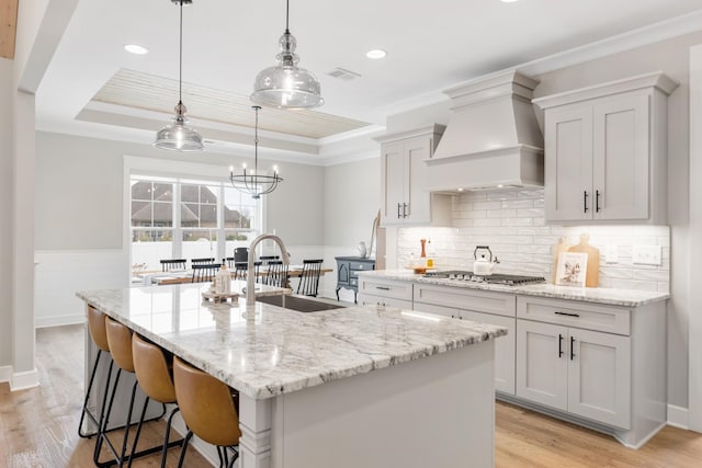 kitchen featuring pendant lighting, a center island with sink, ornamental molding, custom range hood, and stainless steel gas cooktop