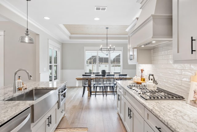 kitchen featuring light stone counters, premium range hood, decorative light fixtures, white cabinets, and appliances with stainless steel finishes