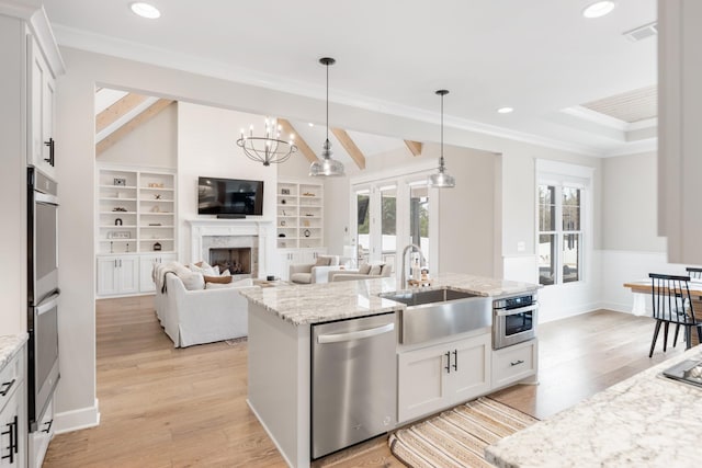 kitchen with appliances with stainless steel finishes, a kitchen island with sink, sink, white cabinetry, and hanging light fixtures