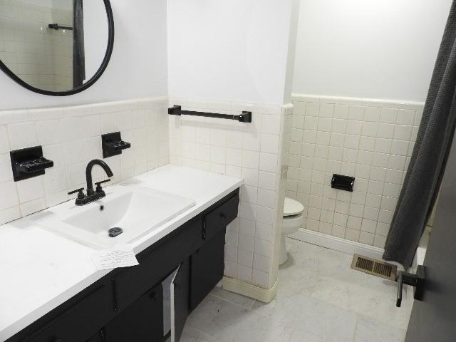 bathroom with tile patterned flooring, vanity, toilet, and tile walls