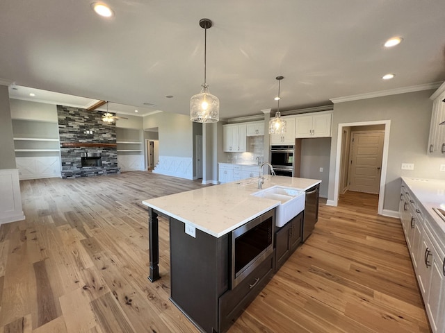 kitchen featuring built in shelves, an island with sink, decorative light fixtures, white cabinetry, and stainless steel appliances