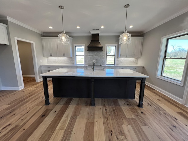 kitchen with a large island with sink, white cabinets, hanging light fixtures, and custom exhaust hood