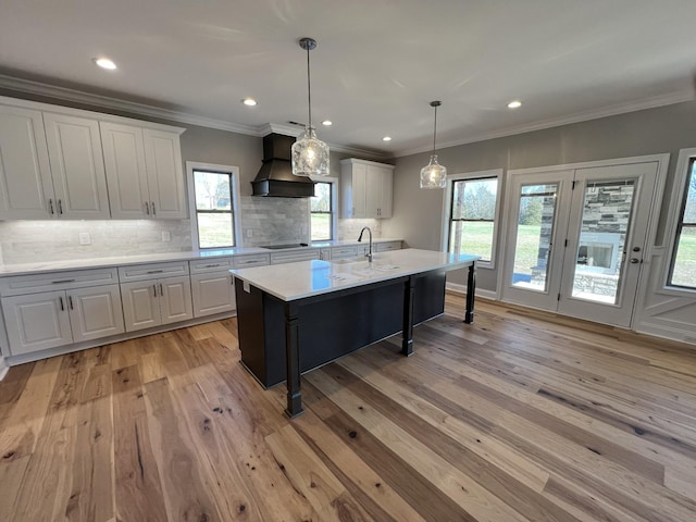 kitchen with custom exhaust hood, black electric cooktop, pendant lighting, a center island with sink, and white cabinets