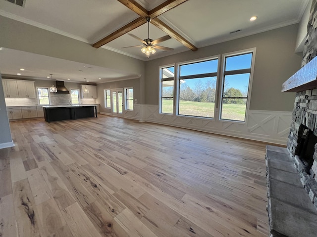 unfurnished living room featuring a stone fireplace, crown molding, ceiling fan, light wood-type flooring, and beamed ceiling