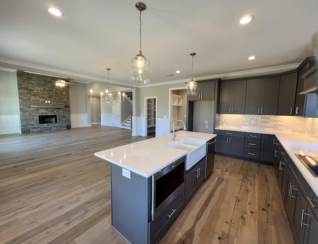 kitchen with a kitchen island with sink, sink, ornamental molding, a fireplace, and stainless steel appliances