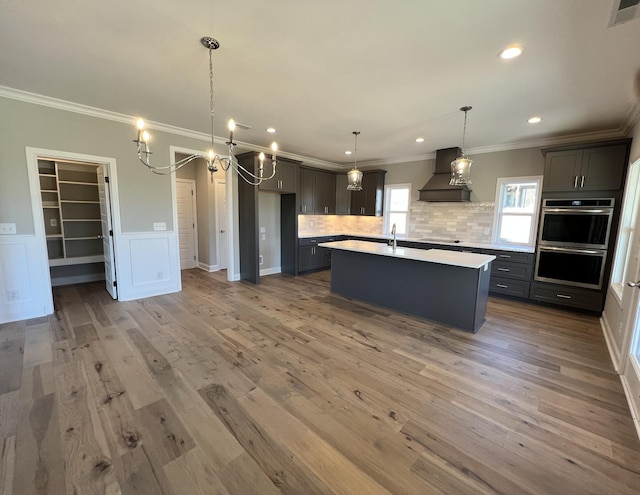 kitchen with tasteful backsplash, custom exhaust hood, pendant lighting, hardwood / wood-style floors, and an island with sink