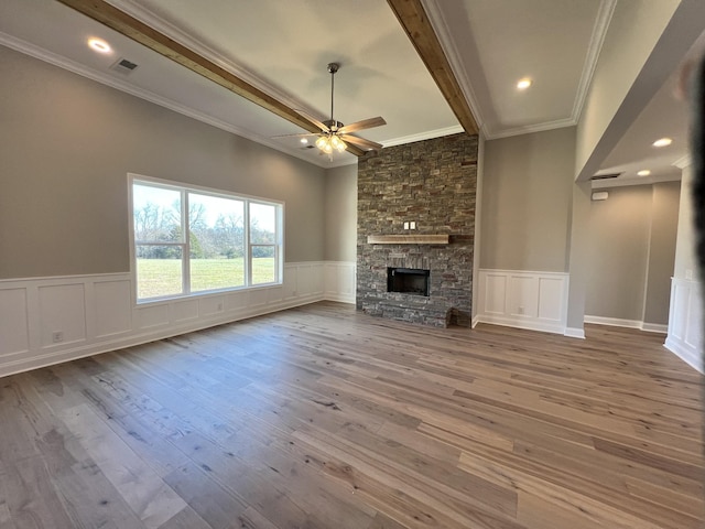 unfurnished living room with a stone fireplace, ceiling fan, ornamental molding, beam ceiling, and wood-type flooring