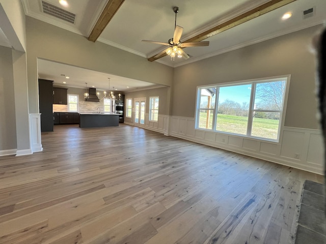 unfurnished living room with beamed ceiling, ceiling fan with notable chandelier, hardwood / wood-style flooring, and crown molding