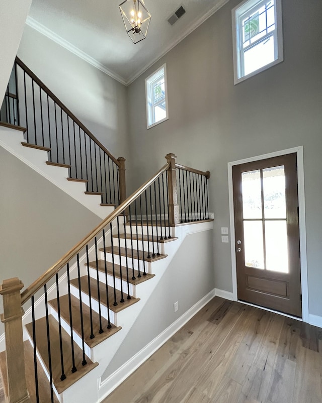 entryway with crown molding, wood-type flooring, and a notable chandelier