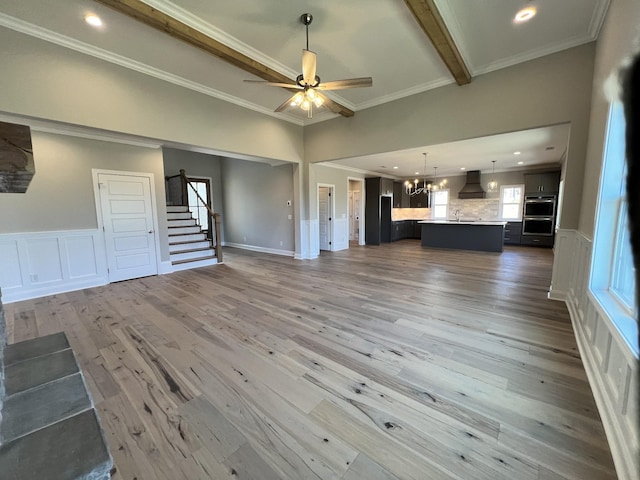 unfurnished living room featuring ceiling fan with notable chandelier, beam ceiling, crown molding, and dark wood-type flooring