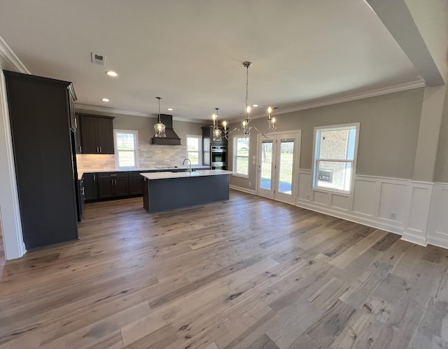 kitchen featuring decorative light fixtures, premium range hood, a center island with sink, and hardwood / wood-style flooring