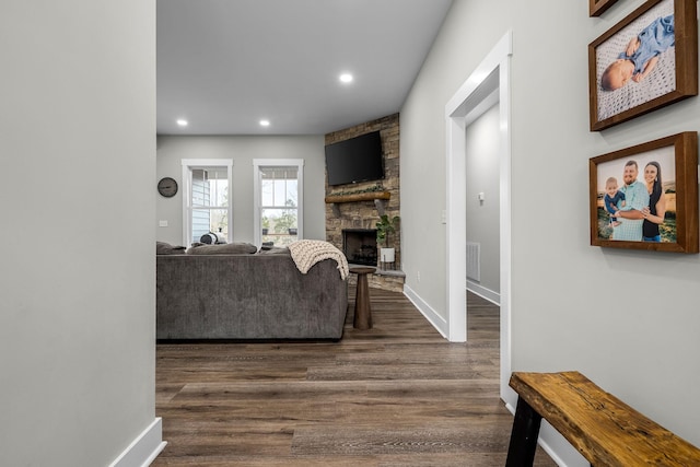 living room featuring a stone fireplace and dark wood-type flooring