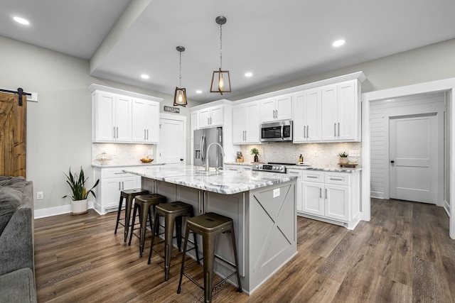 kitchen with stainless steel appliances, a barn door, decorative light fixtures, a kitchen island with sink, and white cabinets