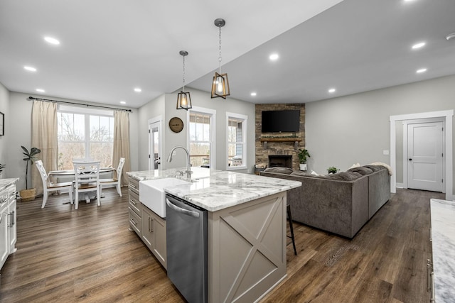 kitchen featuring pendant lighting, dishwasher, a stone fireplace, dark hardwood / wood-style floors, and an island with sink