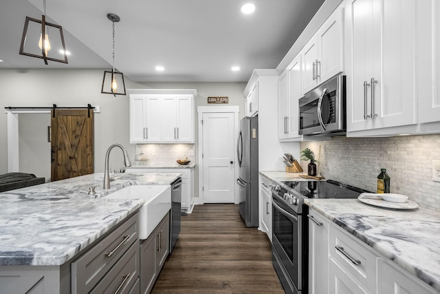 kitchen featuring white cabinets, sink, a barn door, decorative light fixtures, and stainless steel appliances