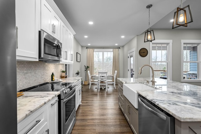 kitchen with appliances with stainless steel finishes, sink, decorative light fixtures, a center island with sink, and white cabinets