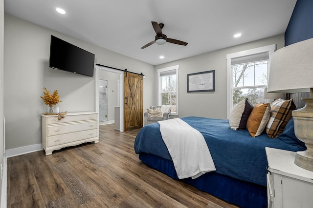 bedroom featuring a barn door, ceiling fan, ensuite bath, and dark wood-type flooring