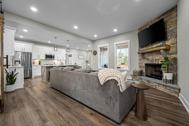 living room with a stone fireplace and dark wood-type flooring