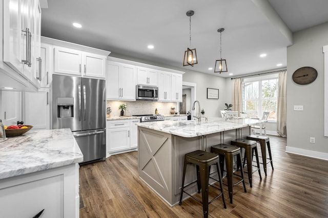 kitchen with decorative light fixtures, white cabinetry, a kitchen island with sink, and appliances with stainless steel finishes