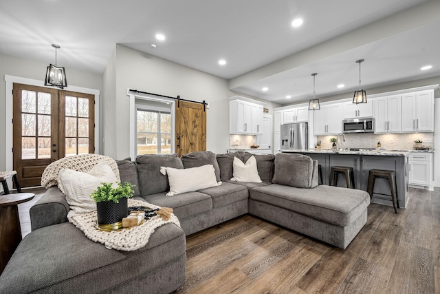 living room featuring a barn door, french doors, dark wood-type flooring, and an inviting chandelier