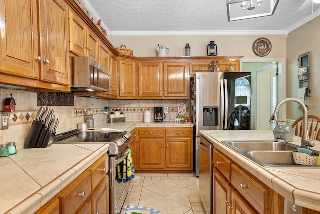 kitchen with tile countertops, ornamental molding, sink, and appliances with stainless steel finishes