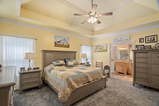 bedroom featuring dark colored carpet, a tray ceiling, ensuite bath, and ceiling fan