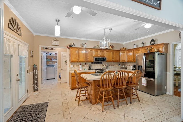 kitchen featuring stainless steel appliances, a textured ceiling, washer / dryer, a center island with sink, and light tile patterned floors