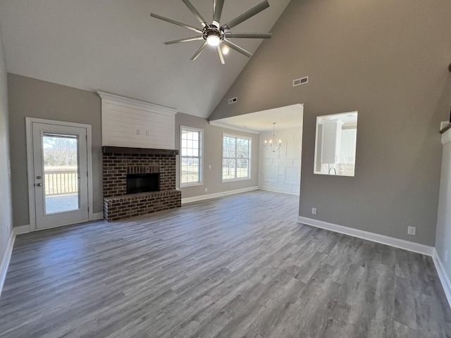 unfurnished living room with a fireplace, high vaulted ceiling, wood-type flooring, and ceiling fan with notable chandelier