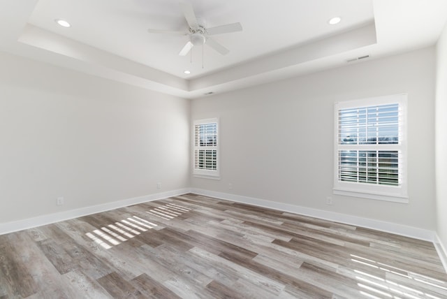 unfurnished room with light wood-type flooring, ceiling fan, and a raised ceiling