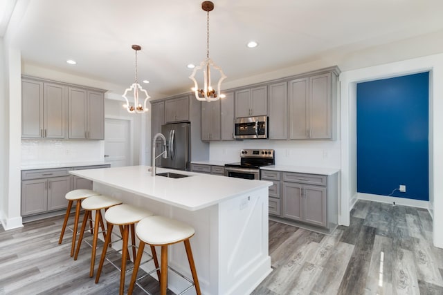 kitchen with gray cabinets, an island with sink, a breakfast bar area, stainless steel appliances, and pendant lighting