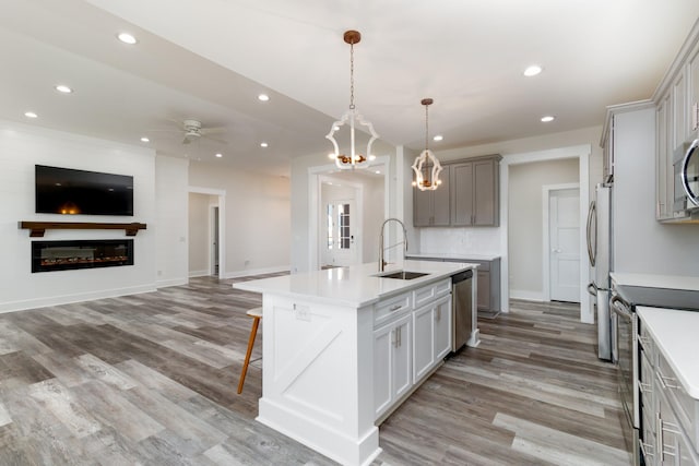 kitchen with gray cabinets, sink, hanging light fixtures, an island with sink, and stainless steel appliances