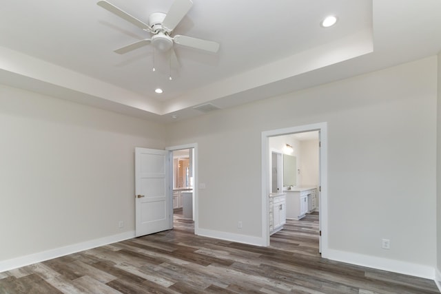 unfurnished bedroom featuring ceiling fan, connected bathroom, a tray ceiling, and dark hardwood / wood-style flooring