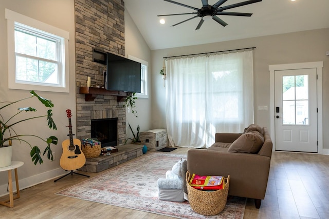 living room with a stone fireplace, ceiling fan, wood-type flooring, and vaulted ceiling