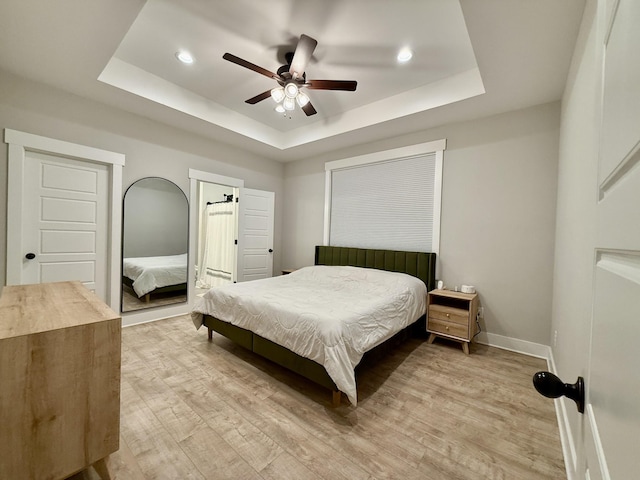 bedroom with light hardwood / wood-style floors, a raised ceiling, and ceiling fan