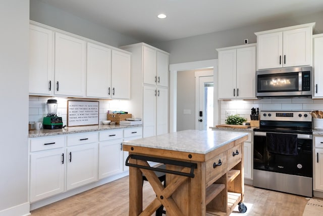 kitchen with white cabinets, appliances with stainless steel finishes, decorative backsplash, and light stone countertops