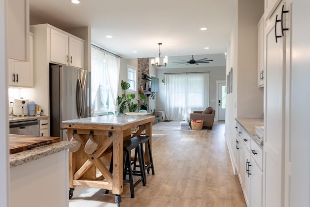 kitchen with appliances with stainless steel finishes, light stone counters, decorative light fixtures, light hardwood / wood-style flooring, and white cabinetry